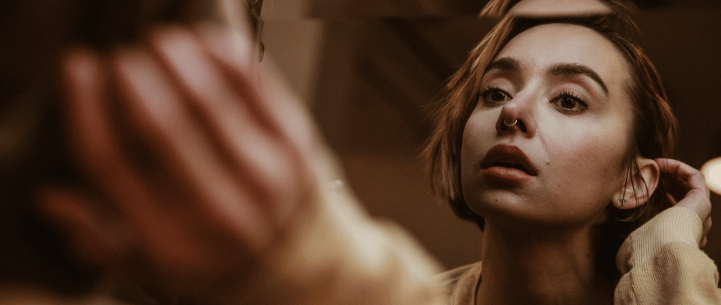 woman looking into a mirror tucking her short hair behind her ear and having a distorted self-image