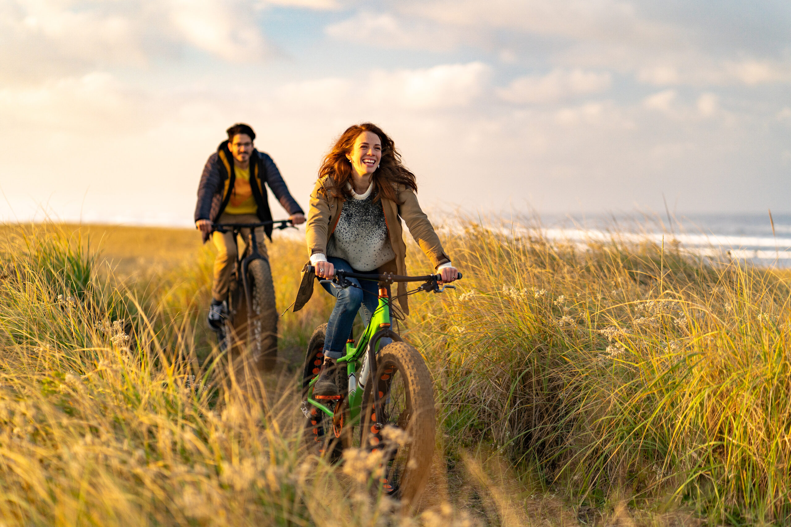 Sun lights up surrounding grassy meadow, Pacific Ocean in distance, couple biking