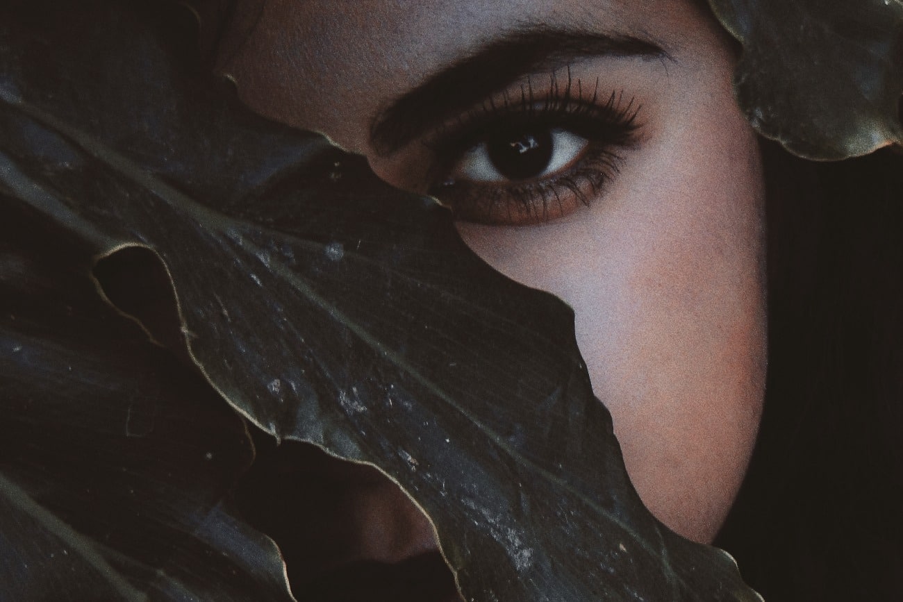 female face hiding behind a leaf