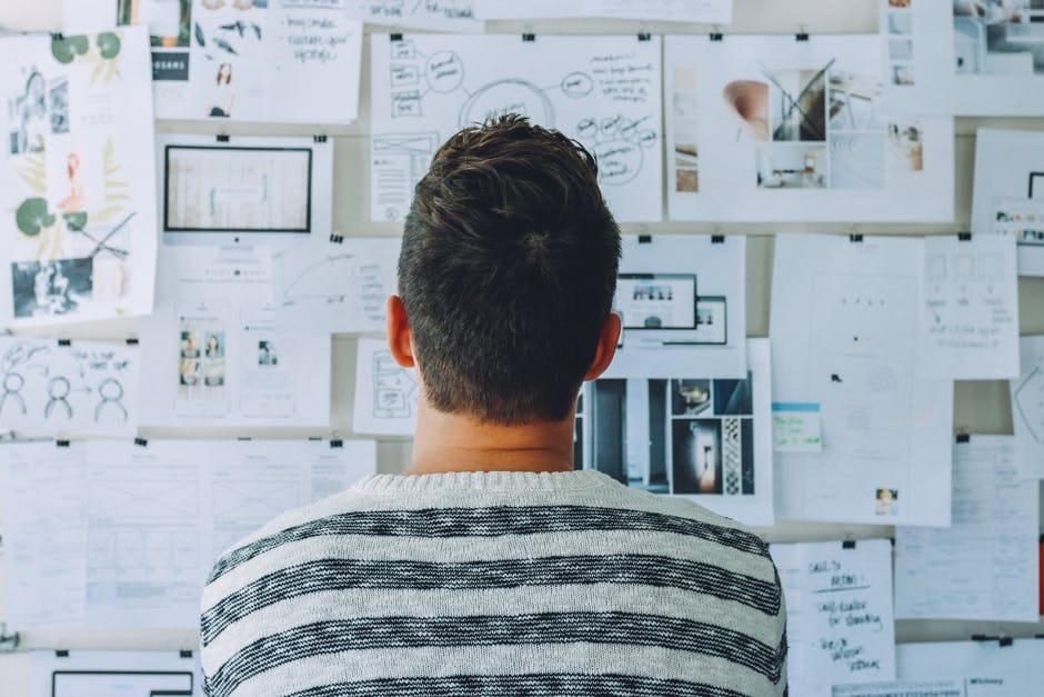 man looking at wall filled with several papers
